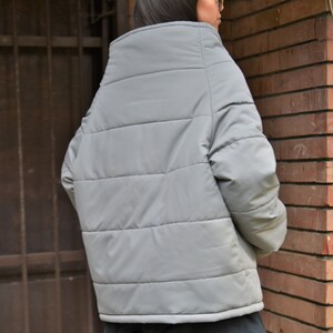 Peut inclure: Une veste matelass&eacute;e grise avec un col montant et une coupe ample.