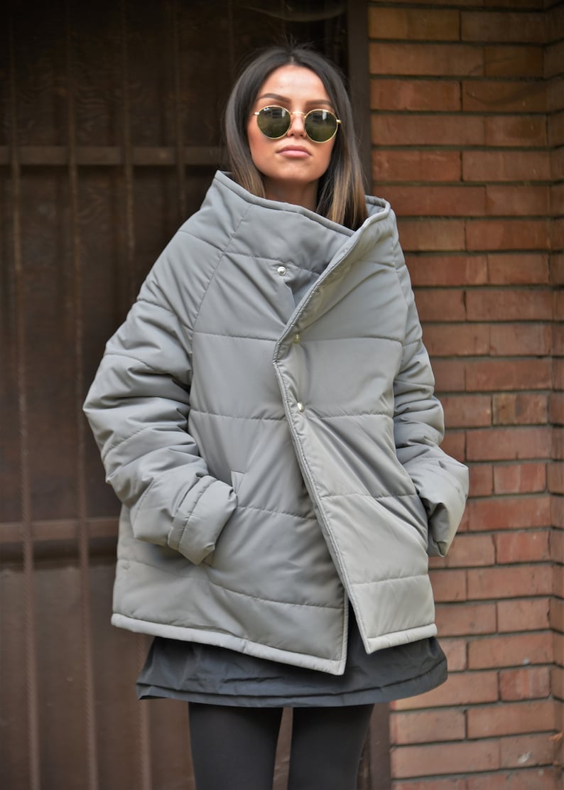 Peut inclure: Une veste matelass&eacute;e grise avec un design asym&eacute;trique unique et un col montant. La veste a une fermeture &agrave; bouton et une texture matelass&eacute;e.