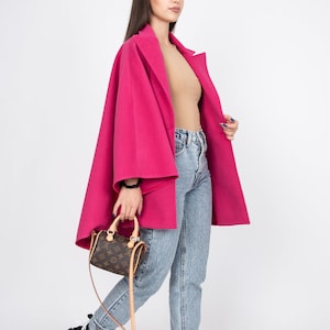 May include: A woman wearing a pink coat, blue jeans, and black and white high-top sneakers. She is carrying a brown leather handbag with a gold chain strap.