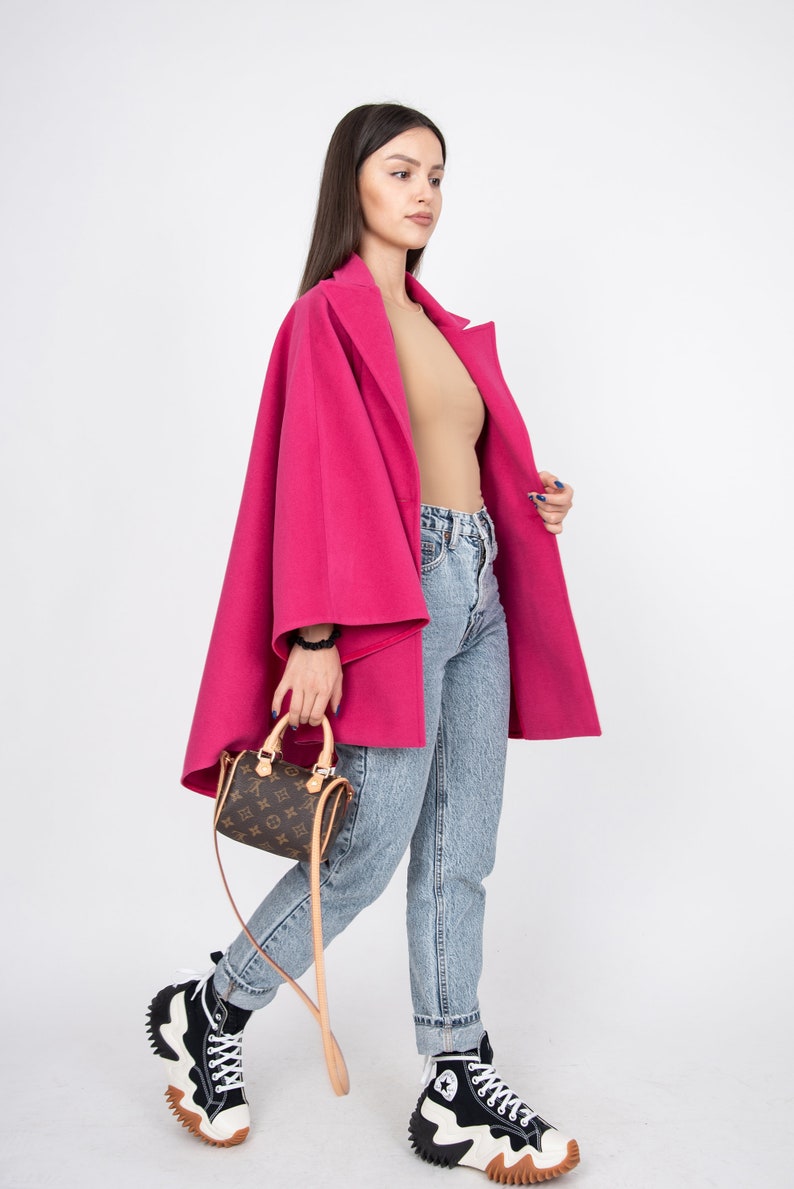 May include: A woman wearing a pink coat, blue jeans, and black and white high-top sneakers. She is carrying a brown leather handbag with a gold chain strap.