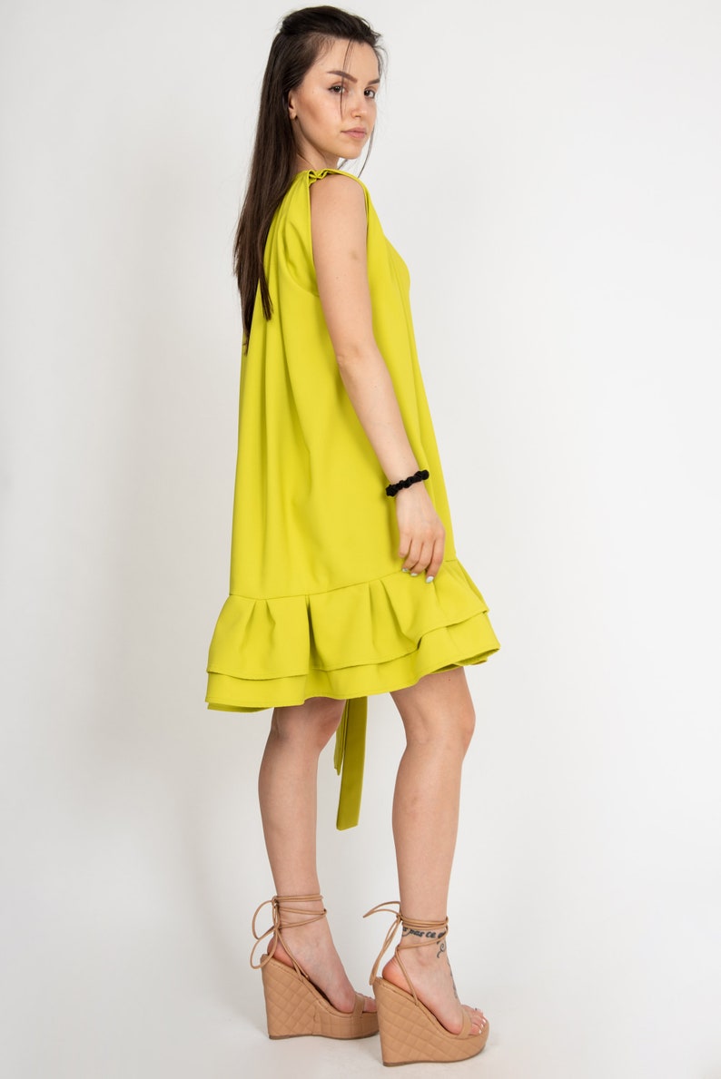 Peut inclure: Une robe sans manches vert citron avec un ourlet &agrave; volants. La robe a une ceinture &agrave; nouer &agrave; la taille et est port&eacute;e avec des sandales compens&eacute;es nudes.