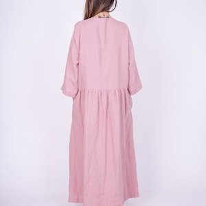 May include: A long, pink linen dress with a gathered waist and 3/4 sleeves. The dress is flowy and has a relaxed fit.