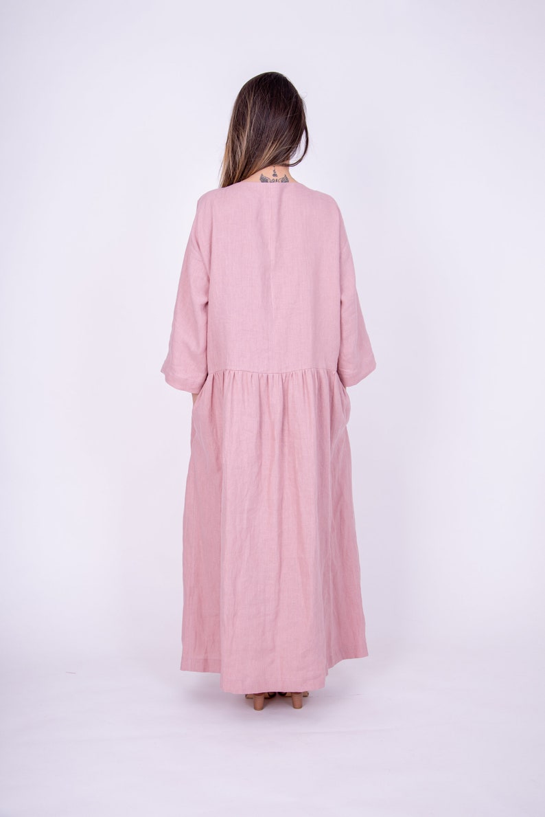 May include: A long, pink linen dress with a gathered waist and 3/4 sleeves. The dress is flowy and has a relaxed fit.