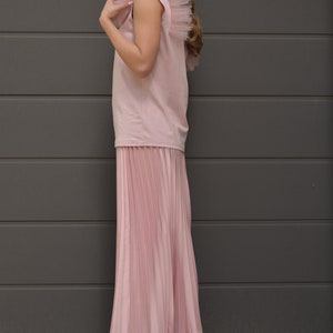 May include: A pink sleeveless top with a tulle ruffle on the shoulder and a pleated pink skirt. The person is wearing white sneakers.