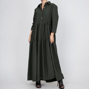 May include: A long, tiered, dark green dress with a button-up front and long sleeves. The dress is made of a soft, flowing fabric and has a relaxed fit.