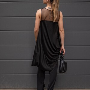 K&ouml;nnte beinhalten: Ein schwarzes &auml;rmelloses Oberteil mit einem durchsichtigen Mesh-Einsatz im R&uuml;cken, kombiniert mit einer schwarzen Hose. Das Oberteil hat einen drapierten, asymmetrischen Schnitt.
