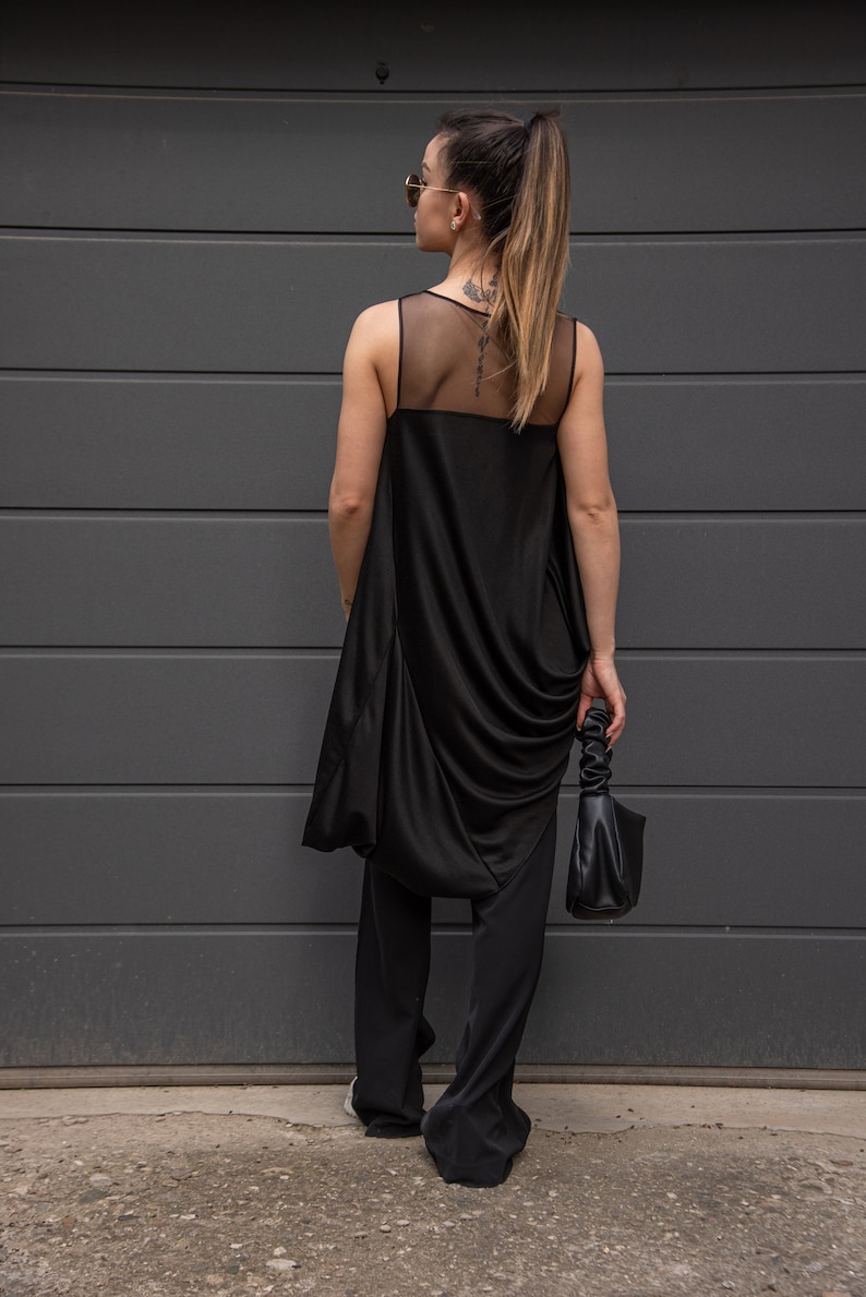K&ouml;nnte beinhalten: Ein schwarzes &auml;rmelloses Oberteil mit einem durchsichtigen Mesh-Einsatz im R&uuml;cken, kombiniert mit einer schwarzen Hose. Das Oberteil hat einen drapierten, asymmetrischen Schnitt.