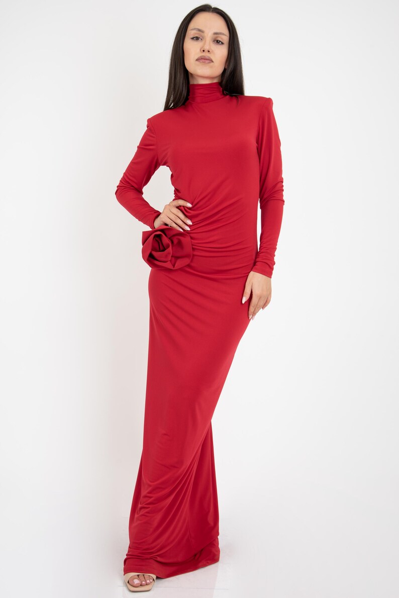 May include: A long red dress with a high neck and a large flower detail on the side.