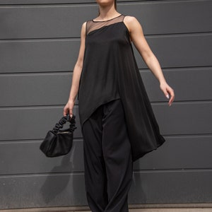 K&ouml;nnte beinhalten: Eine Frau tr&auml;gt ein schwarzes &auml;rmelloses Oberteil mit einem durchsichtigen Einsatz und eine schwarze weite Hose. Sie tr&auml;gt eine kleine schwarze Handtasche und wei&szlig;e Turnschuhe.