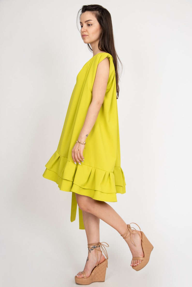Peut inclure: Une robe sans manches vert citron avec un ourlet &agrave; volants et une ceinture &agrave; la taille. La robe est port&eacute;e par une personne aux cheveux longs bruns et est associ&eacute;e &agrave; des sandales compens&eacute;es beiges.