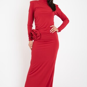 May include: A long, red dress with a high neck and a large flower detail on the side. The dress is made of a stretchy, form-fitting fabric.
