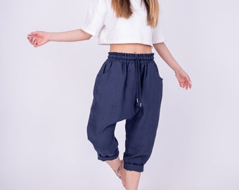 May include: A woman wearing a white cropped top and dark blue linen pants with a drawstring waist.