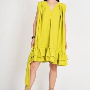 Peut inclure: Une robe sans manches vert citron avec un ourlet &agrave; volants. La robe a un col en V et un d&eacute;tail pliss&eacute; aux &eacute;paules. Le mannequin porte la robe avec des sandales &agrave; talons marrons.