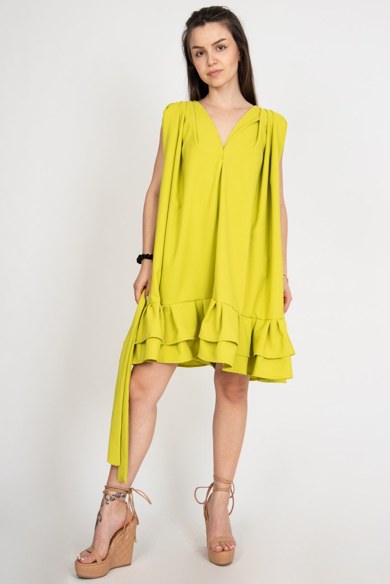 Peut inclure: Une robe sans manches vert citron avec un ourlet &agrave; volants. La robe a un col en V et un d&eacute;tail pliss&eacute; aux &eacute;paules. Le mannequin porte la robe avec des sandales &agrave; talons marrons.