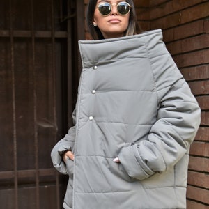 Peut inclure: Une veste matelass&eacute;e grise avec un col montant et une fermeture &agrave; bouton unique. La veste a une coupe ample et est matelass&eacute;e sur toute sa surface.