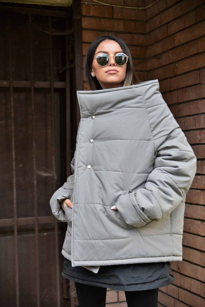 Peut inclure: Une veste matelass&eacute;e grise avec un col montant et une fermeture &agrave; bouton unique. La veste a une coupe ample et est matelass&eacute;e sur toute sa surface.