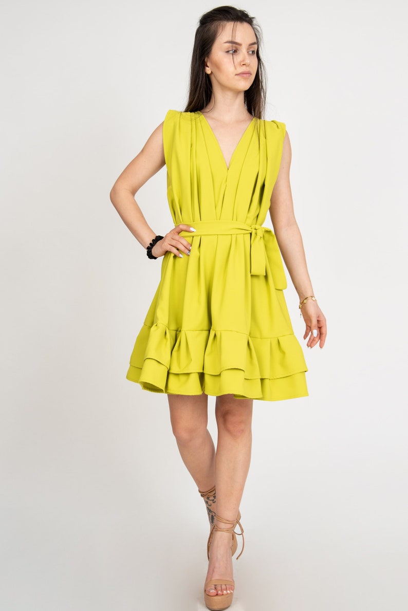 Peut inclure: Une robe jaune vif sans manches avec un d&eacute;collet&eacute; en V, une ceinture &agrave; nouer &agrave; la taille et un ourlet &agrave; volants.