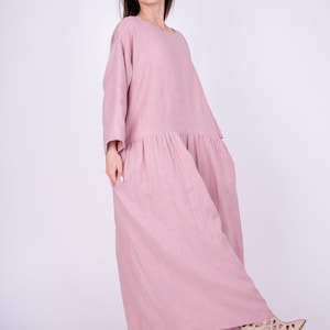May include: A long, loose-fitting, dusty rose linen dress with a gathered skirt and 3/4 sleeves.