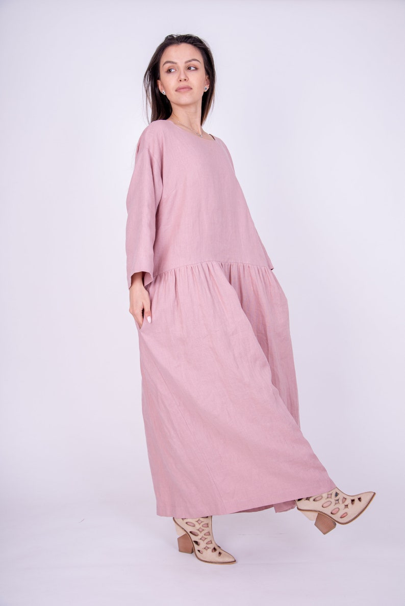 May include: A long, loose-fitting, dusty rose linen dress with a gathered skirt and 3/4 sleeves.