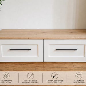 May include: A low rectangular storage unit with a natural light wood top and two white drawers featuring black horizontal bar handles. Below the unit, text icons read: SOLID WOOD BUILT TO LAST, CUSTOM SIZES MADE TO FIT YOUR SPACE, MULTIPLE FINISHES CHOOSE YOUR STYLE, HANDMADE MADE WITH CARE.