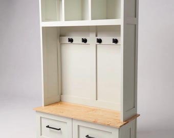 May include: A white hall tree featuring a natural wood bench seat, two lower drawers with black handles, and an upper section with three open storage cubbies. The back panel includes four black coat hooks mounted on a vertical frame structure.