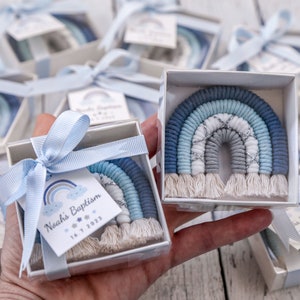 Op de afbeelding: Een set kleine witte doosjes met blauwe strikken, elk met een blauwe en witte regenboog van garen en een wit label met de tekst "Noah's Doop 16.7.2023".