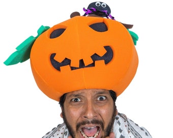 May include: A man wearing a bright orange pumpkin hat with a black spider on top. He is looking at the camera with a scared expression and his hands are covering his face.