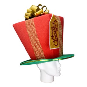 Peut inclure: Un chapeau de No&euml;l fantaisie en forme de cadeau emball&eacute;. Le chapeau rouge est orn&eacute; de rubans dor&eacute;s et d'un n&oelig;ud dor&eacute;. Une &eacute;tiquette dor&eacute;e avec "Merry Christmas" est attach&eacute;e. Le chapeau a un bord vert.