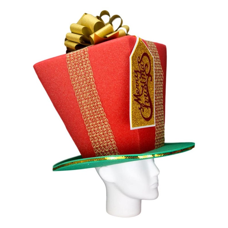 Peut inclure: Un chapeau de No&euml;l fantaisie en forme de cadeau emball&eacute;. Le chapeau rouge est orn&eacute; de rubans dor&eacute;s et d'un n&oelig;ud dor&eacute;. Une &eacute;tiquette dor&eacute;e avec "Merry Christmas" est attach&eacute;e. Le chapeau a un bord vert.