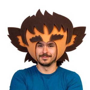 May include: A foam headpiece featuring a stylized character design with dark brown hair, pointed ears, and thick eyebrows. The mask is constructed from orange and brown foam, designed to frame the face with a wide, jagged, and layered aesthetic.