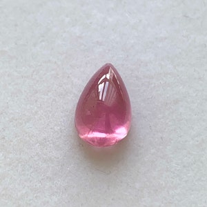 K&ouml;nnte beinhalten: Ein tropfenf&ouml;rmiger rosa Edelstein mit einer glatten, polierten Oberfl&auml;che.