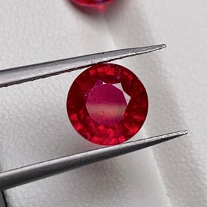 Peut inclure: Deux pierres précieuses rondes de couleur rouge. La plus grande pierre est tenue dans une pince, tandis que la plus petite est posée sur une surface blanche.