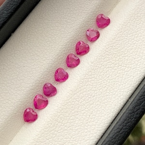 Könnte beinhalten: Eine Reihe von acht rosafarbenen herzförmigen Edelsteinen in einer weiß samtenen Box.