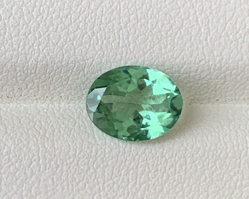 May include: A light green oval-shaped gemstone with facets.