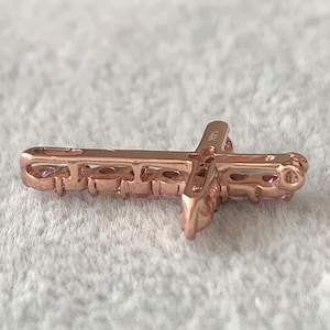 May include: A rose gold cross pendant with small pink gemstones set around the edges. The pendant is marked "14K" on the back.