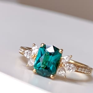 Pode incluir: Um anel de ouro com uma grande gema verde esmeralda cercada por gemas menores e transparentes.