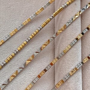 May include: Four gold and silver chain bracelets with square links. The chains are arranged in a diagonal pattern on a white background.