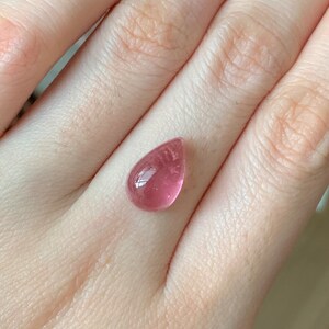 K&ouml;nnte beinhalten: Ein tropfenf&ouml;rmiger rosa Edelstein mit einer glatten, polierten Oberfl&auml;che.