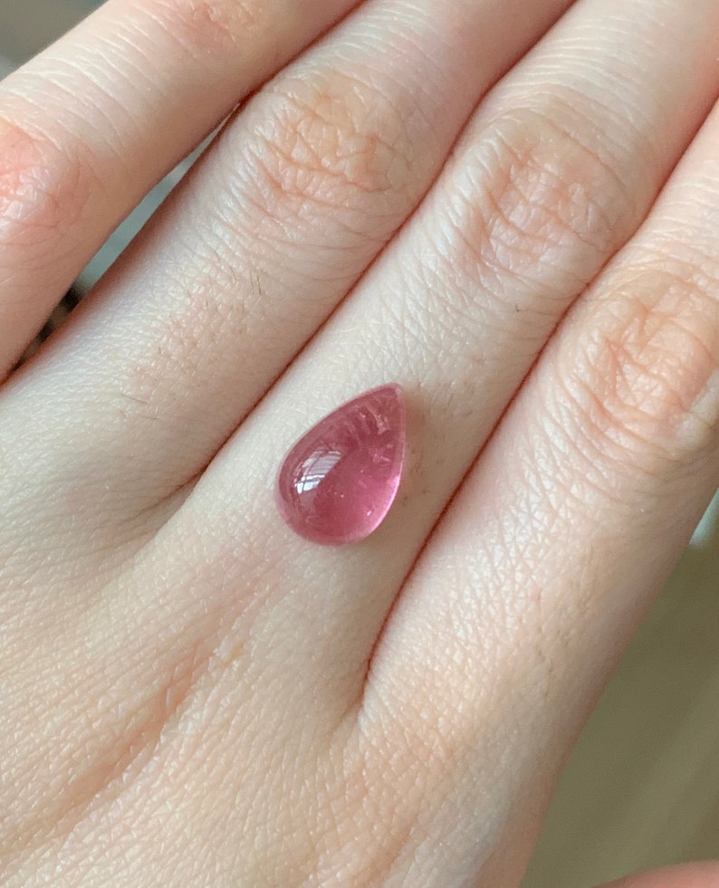 K&ouml;nnte beinhalten: Ein tropfenf&ouml;rmiger rosa Edelstein mit einer glatten, polierten Oberfl&auml;che.