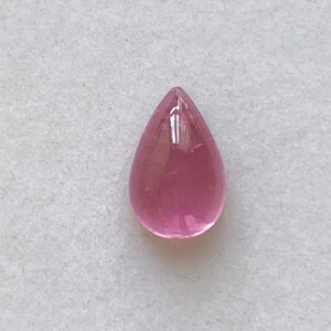 K&ouml;nnte beinhalten: Ein tropfenf&ouml;rmiger rosa Edelstein mit einer glatten, polierten Oberfl&auml;che.