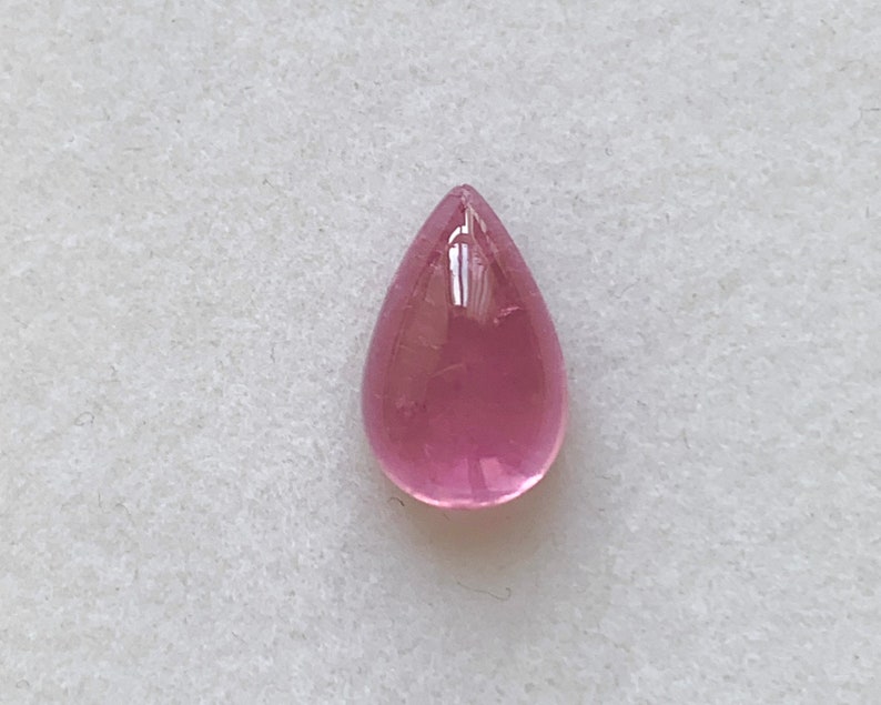 K&ouml;nnte beinhalten: Ein tropfenf&ouml;rmiger rosa Edelstein mit einer glatten, polierten Oberfl&auml;che.