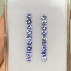 May include: Two rows of round, faceted, purple gemstones in a clear plastic display case.