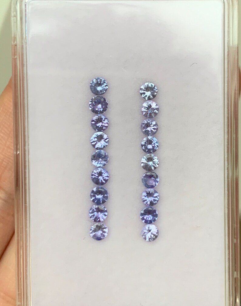May include: Two rows of round, faceted, purple gemstones in a clear plastic display case.