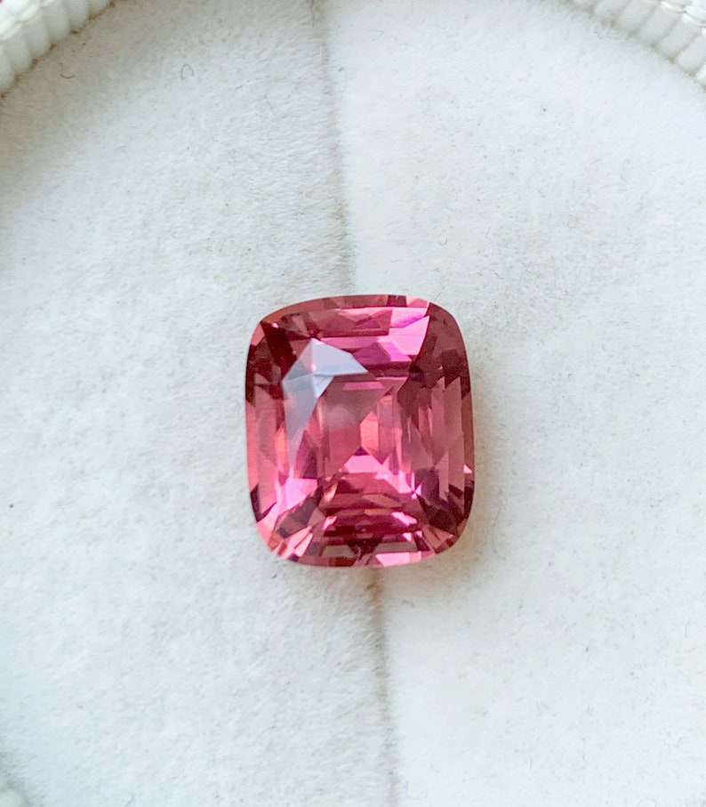 Puede incluir: Una piedra preciosa rosa con un corte de coj&iacute;n. La piedra preciosa est&aacute; engastada en un engaste blanco.
