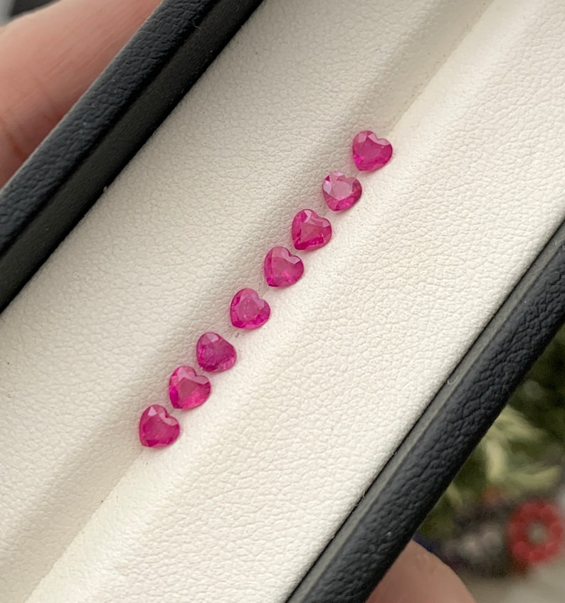 May include: A row of eight pink heart-shaped gemstones in a white velvet-lined box.
