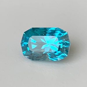 Puede incluir: Una gema azul vibrante con una forma octogonal facetada. La gema tiene una apariencia clara y vidriosa y refleja la luz maravillosamente.
