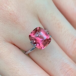 Puede incluir: Un anillo con una gran piedra preciosa rosa de talla coj&iacute;n engastada en una banda plateada.