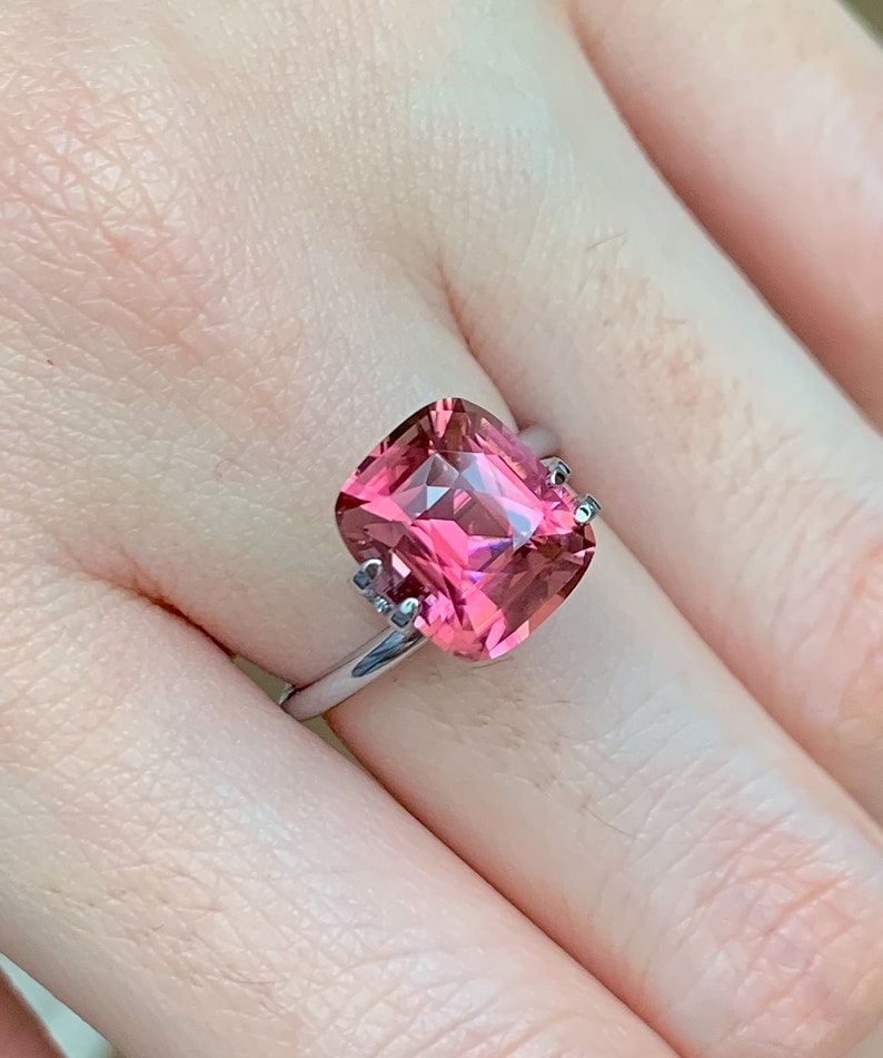 Puede incluir: Un anillo con una gran piedra preciosa rosa de talla coj&iacute;n engastada en una banda plateada.