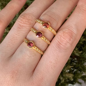 May include: Three gold rings with a single round red gemstone and a band of small white gemstones.