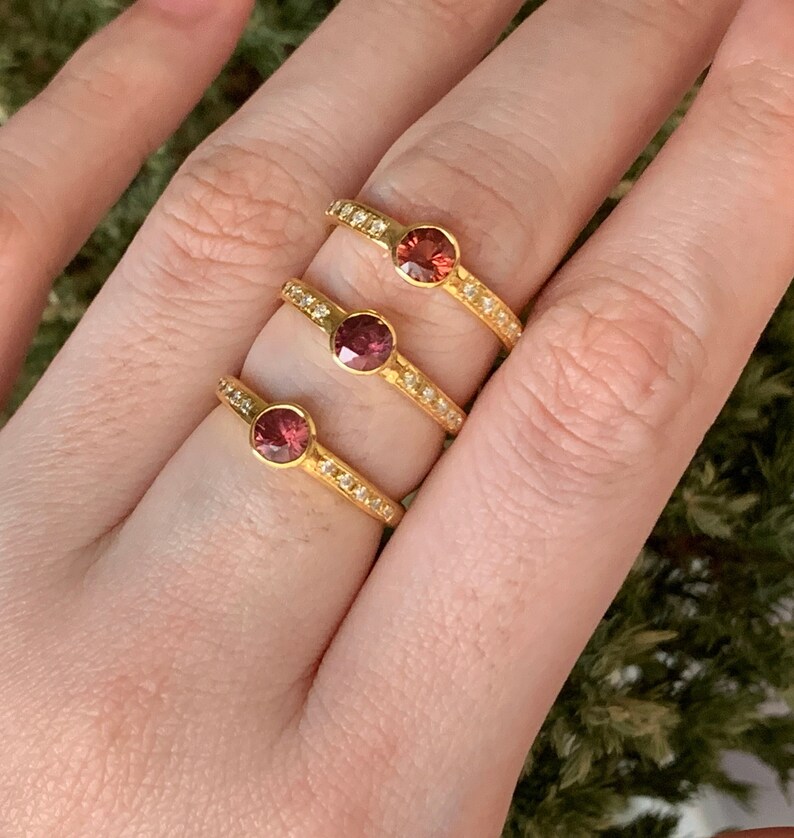 May include: Three gold rings with a single round red gemstone and a band of small white gemstones.